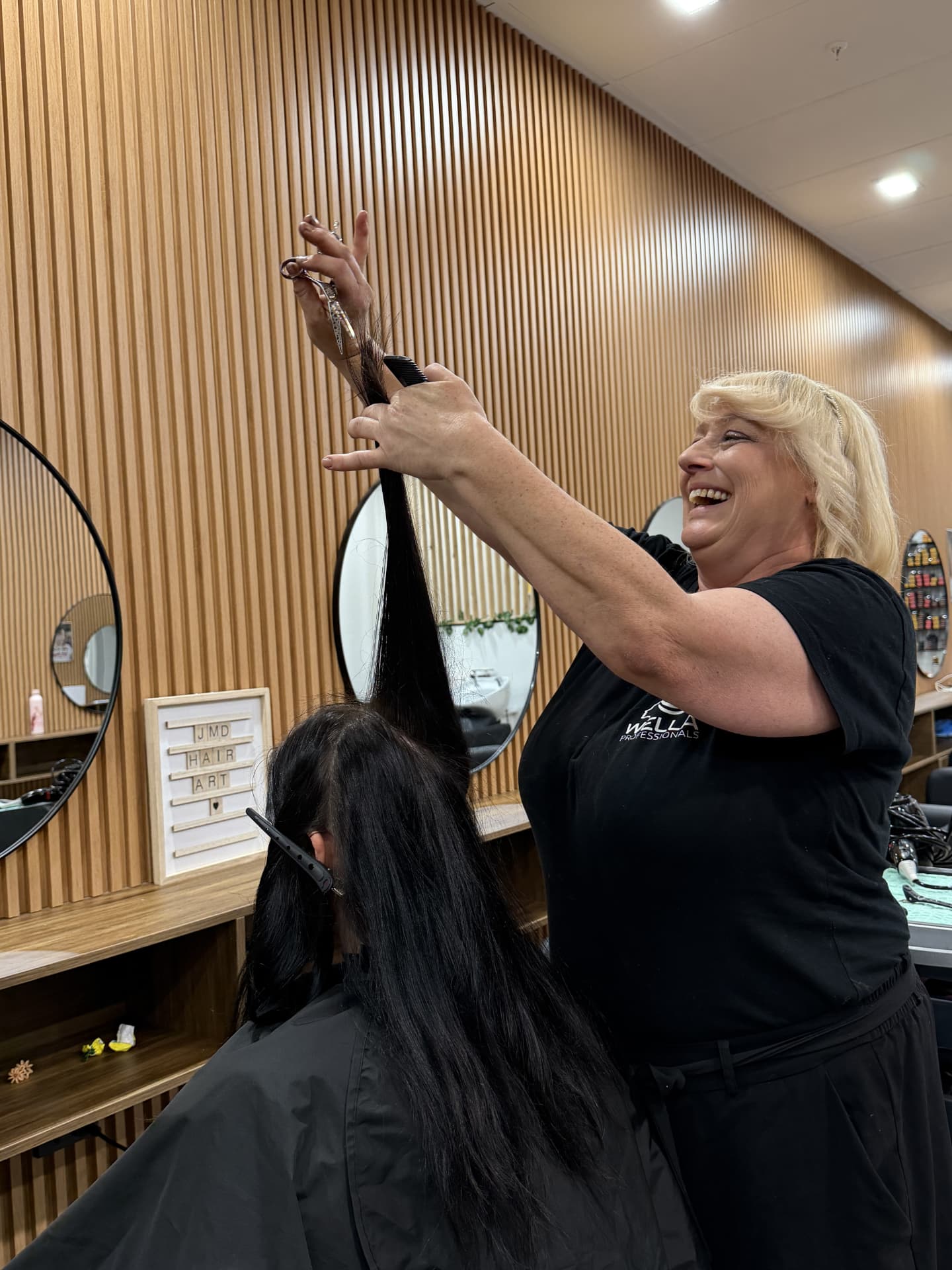 JMD Hair Art stylist smiling while cutting long black hair in salon